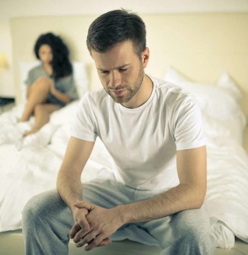 sad man sitting on the bed with woman behind him